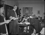 The ceremony of signing 'the Book of the College' was held at the University of Western Australia Hostel 13 April 1950. The honorary tutor in psychology Dr E. Morey is signing while the secretary of the University Women's College Council Mrs E. M. Watson (seated) looks on [picture]