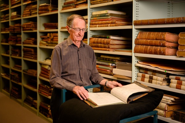 A volunteer examining heritage material in a room full of books