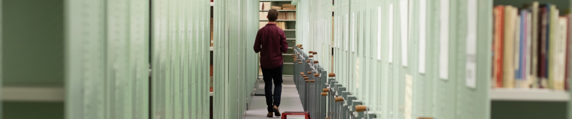 A staff member walking down a row of compactus storage units in the STAX area